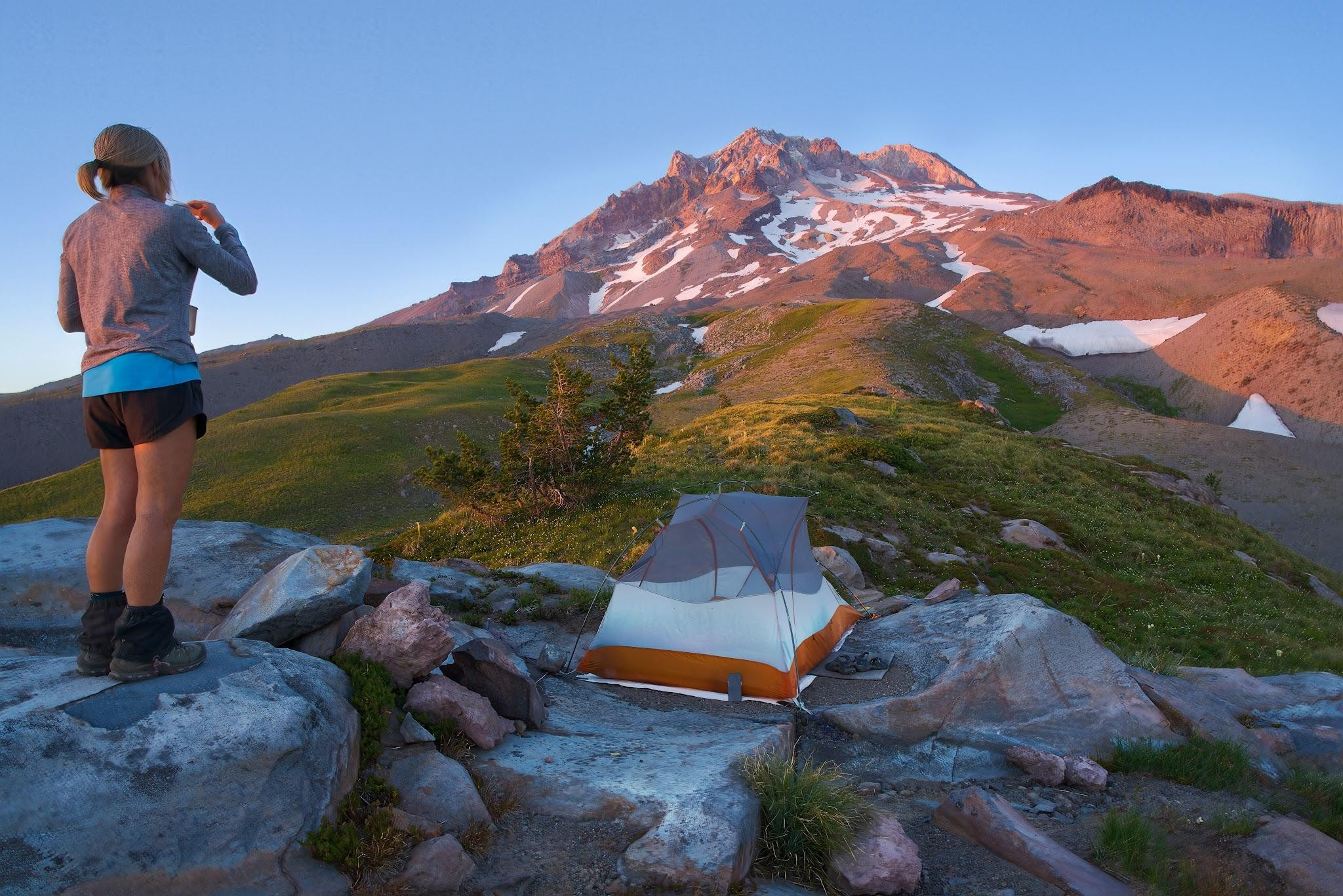 A woman enjoys camping at sunrise with a mountain view 4 Easy Tricks for Easy Camp Mornings: A woman enjoys camping at sunrise with a mountain view.